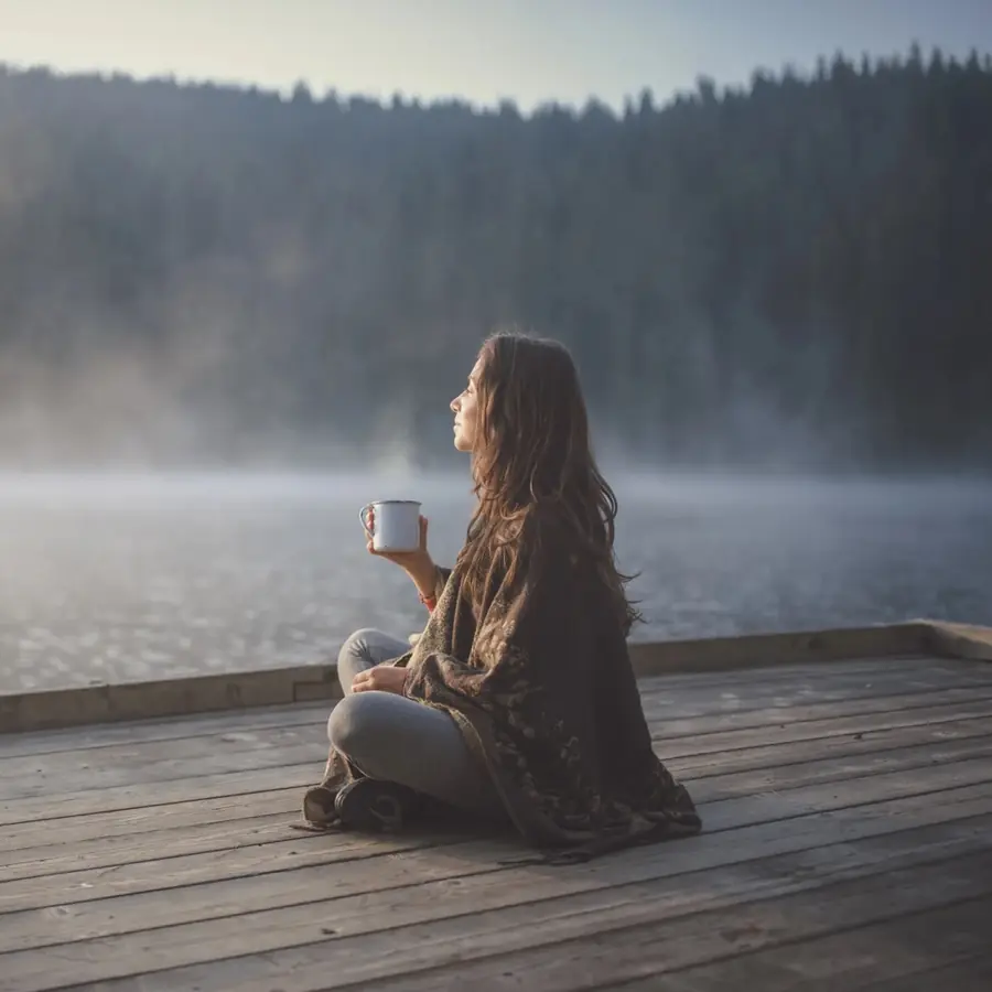 Woman on dock on a misty morning with a coffee